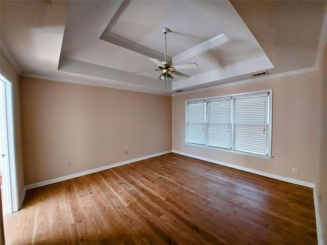 empty room featuring a raised ceiling, crown molding, and hardwood / wood-style flooring