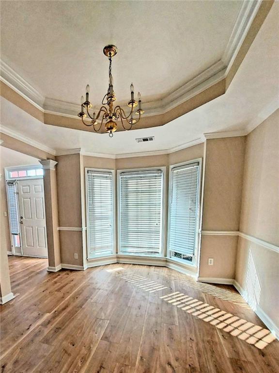 unfurnished dining area featuring an inviting chandelier, hardwood / wood-style flooring, ornamental molding, a tray ceiling, and a healthy amount of sunlight