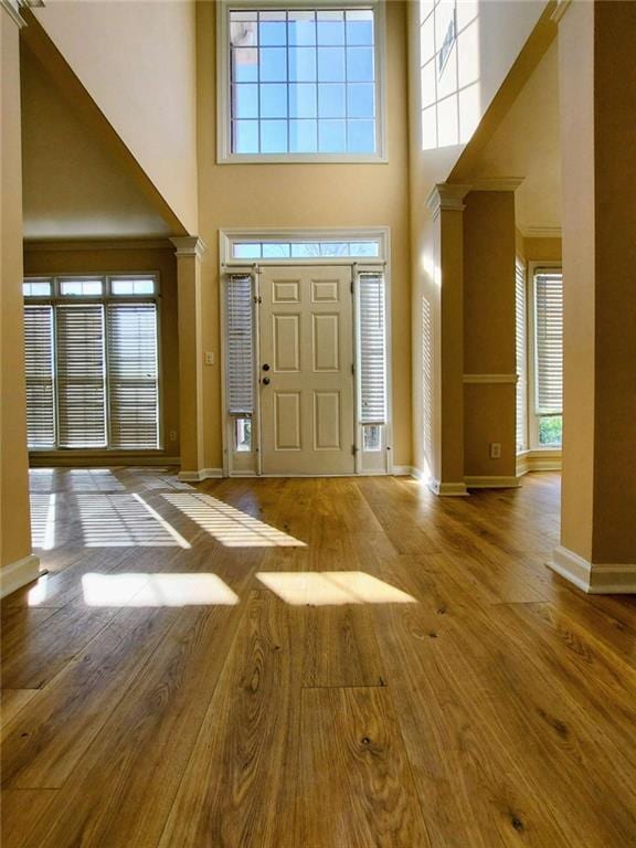 foyer entrance featuring decorative columns, a high ceiling, and light wood-type flooring