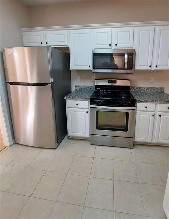 kitchen with dark stone countertops, white cabinetry, light tile patterned floors, and appliances with stainless steel finishes