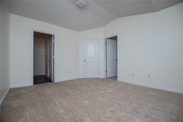 carpeted empty room featuring vaulted ceiling and baseboards