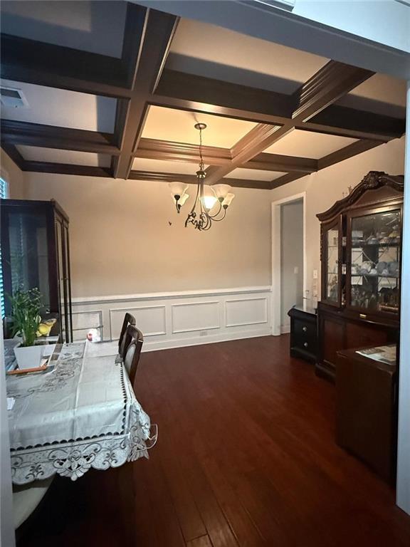 dining space with coffered ceiling, a chandelier, beamed ceiling, dark wood-style floors, and wainscoting