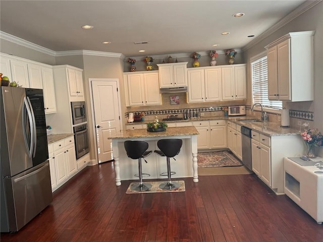 kitchen featuring stainless steel appliances, a sink, a kitchen island, a breakfast bar area, and backsplash