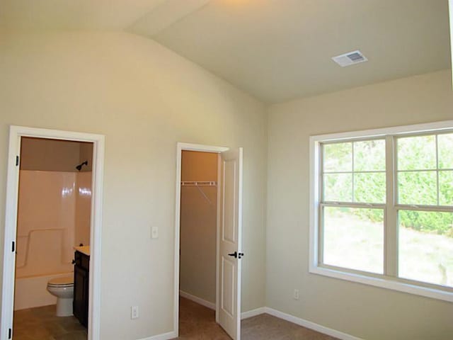 unfurnished bedroom with a spacious closet, vaulted ceiling, multiple windows, and baseboards