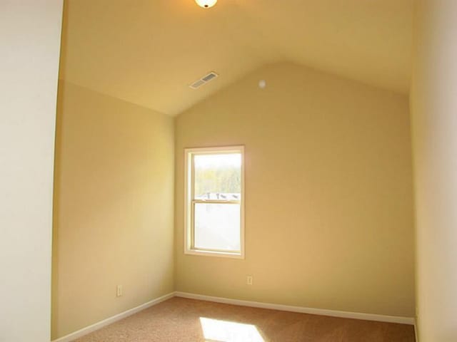 carpeted empty room featuring vaulted ceiling and baseboards