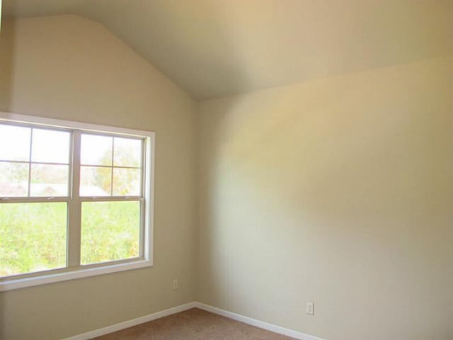 empty room featuring vaulted ceiling, light colored carpet, baseboards, and plenty of natural light