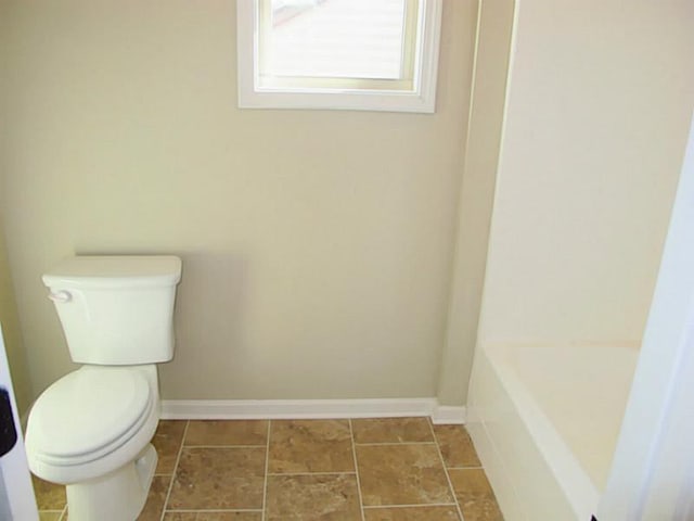 bathroom featuring toilet, baseboards, and a tub to relax in