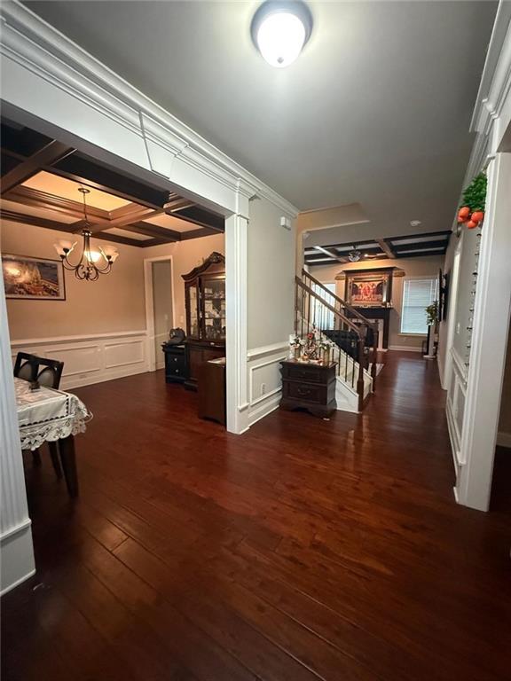 corridor featuring stairs, a decorative wall, wood finished floors, a chandelier, and a wainscoted wall