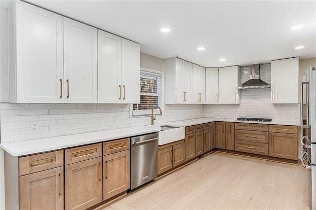 kitchen featuring light countertops, light wood-style flooring, appliances with stainless steel finishes, a sink, and wall chimney range hood