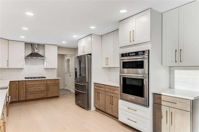 kitchen featuring tasteful backsplash, stainless steel appliances, light countertops, light wood-type flooring, and wall chimney range hood