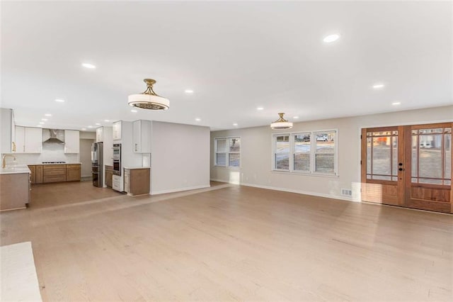 unfurnished living room featuring light wood finished floors, french doors, a sink, and recessed lighting