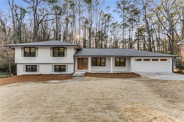 tri-level home with concrete driveway, brick siding, an attached garage, and roof with shingles