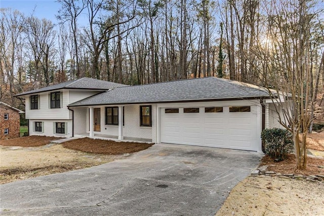 tri-level home featuring an attached garage, driveway, a shingled roof, and brick siding