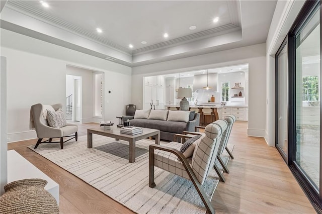 living area featuring a raised ceiling, crown molding, recessed lighting, and light wood-style flooring