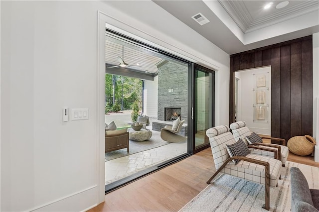 doorway featuring visible vents, ornamental molding, a fireplace, wood finished floors, and wood walls