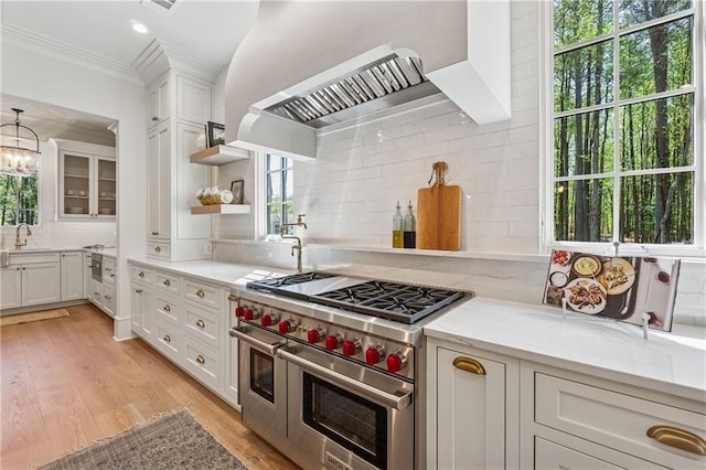 kitchen with white cabinetry, light wood finished floors, wall chimney range hood, and range with two ovens