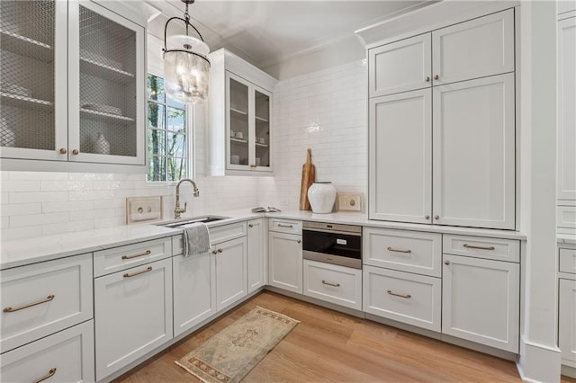 kitchen featuring white cabinets, decorative light fixtures, a sink, backsplash, and light wood-style flooring