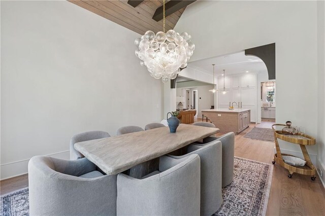 dining area with a notable chandelier, vaulted ceiling, light wood-style floors, arched walkways, and wooden ceiling