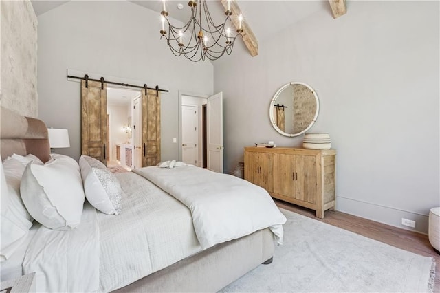 bedroom featuring a notable chandelier, a barn door, connected bathroom, wood finished floors, and high vaulted ceiling