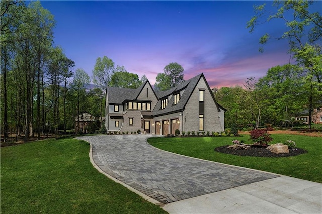 tudor-style house featuring an attached garage, decorative driveway, and a front lawn