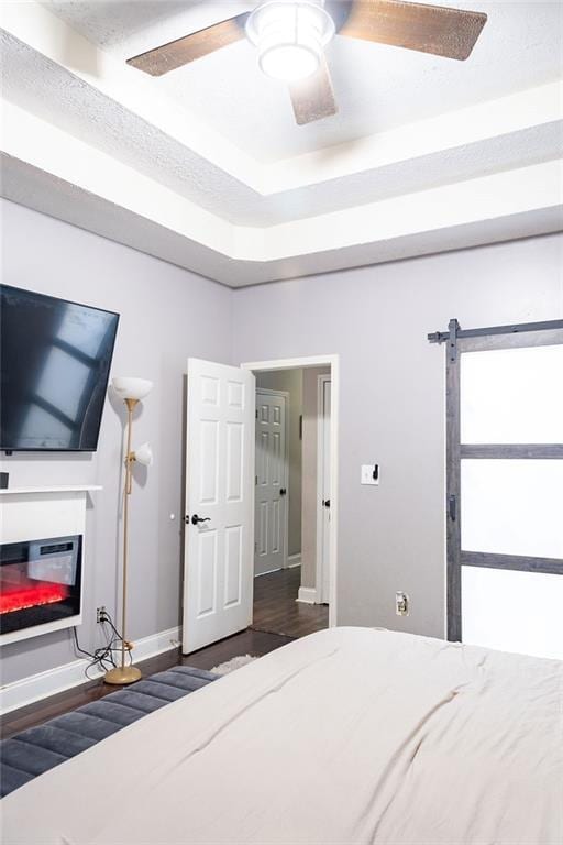 bedroom with dark wood-type flooring, a raised ceiling, and ceiling fan