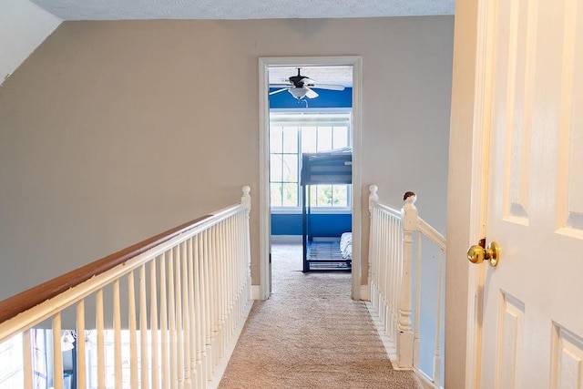 hallway with vaulted ceiling, light colored carpet, and a textured ceiling