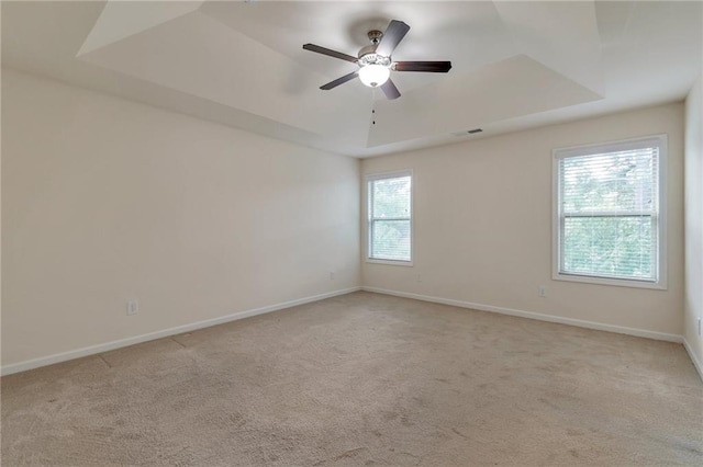 carpeted spare room featuring a wealth of natural light, ceiling fan, and a raised ceiling