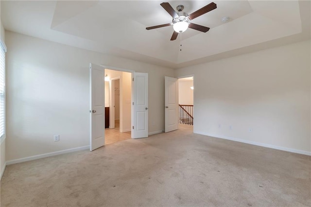 unfurnished bedroom featuring ceiling fan, light carpet, and a raised ceiling