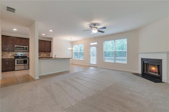 unfurnished living room with light colored carpet, sink, and ceiling fan with notable chandelier