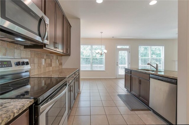 kitchen with appliances with stainless steel finishes, backsplash, an inviting chandelier, light stone countertops, and light tile patterned floors