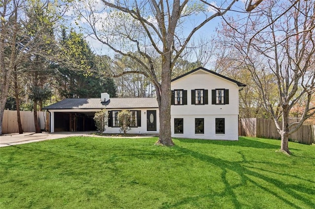 back of house featuring concrete driveway, a carport, fence, and a lawn