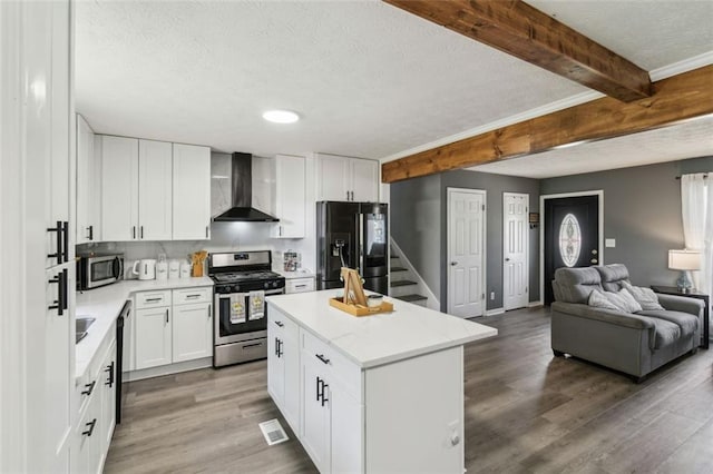 kitchen featuring wood finished floors, stainless steel appliances, beam ceiling, and wall chimney exhaust hood