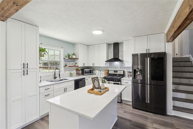 kitchen with wood finished floors, stainless steel appliances, a kitchen island, a sink, and wall chimney range hood