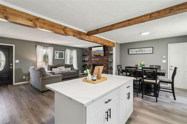 kitchen with white cabinetry, a brick fireplace, a textured ceiling, light wood-style flooring, and beamed ceiling
