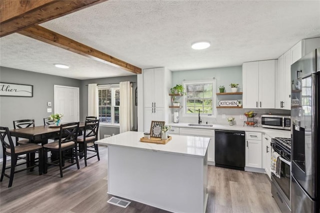 kitchen with light countertops, open shelves, stainless steel appliances, a sink, and wood finished floors