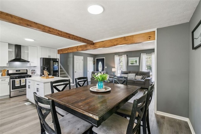 dining space featuring stairway, light wood-type flooring, baseboards, a textured ceiling, and beamed ceiling