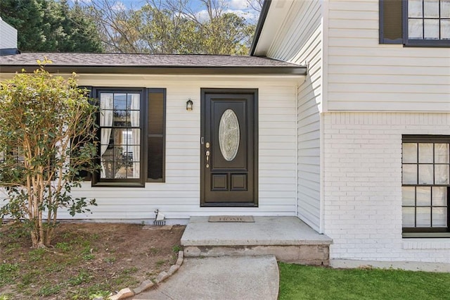 entrance to property featuring brick siding and roof with shingles