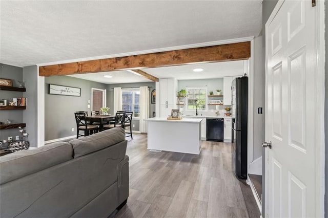 living room featuring a textured ceiling, baseboards, beamed ceiling, and light wood-type flooring