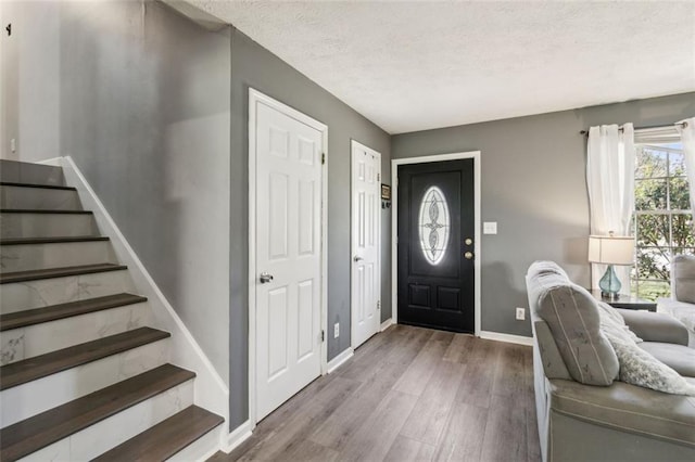 entryway featuring a textured ceiling, baseboards, stairs, and wood finished floors