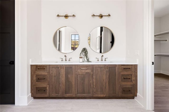 bathroom featuring double vanity, baseboards, a sink, and wood finished floors