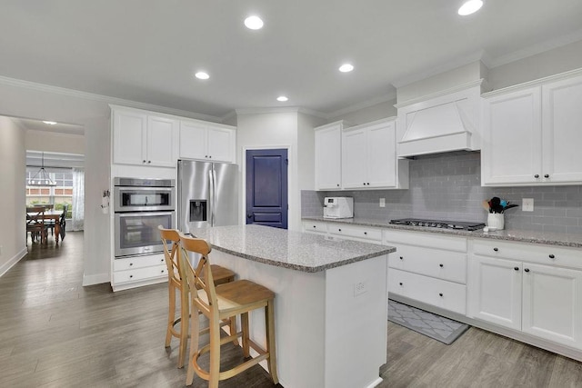 7190 Tributary Ct, Cumming, GA 30040 - kitchen featuring appliances with stainless steel finishes, ornamental molding, a kitchen island, wood finished floors, and decorative backsplash