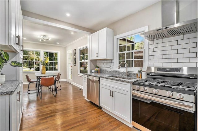 kitchen featuring wall chimney exhaust hood, white cabinetry, stainless steel appliances, sink, and light stone counters