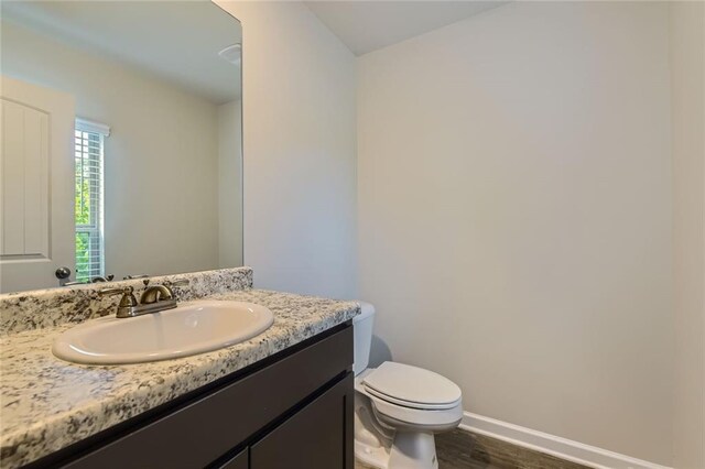 half bathroom featuring toilet, baseboards, wood finished floors, and vanity