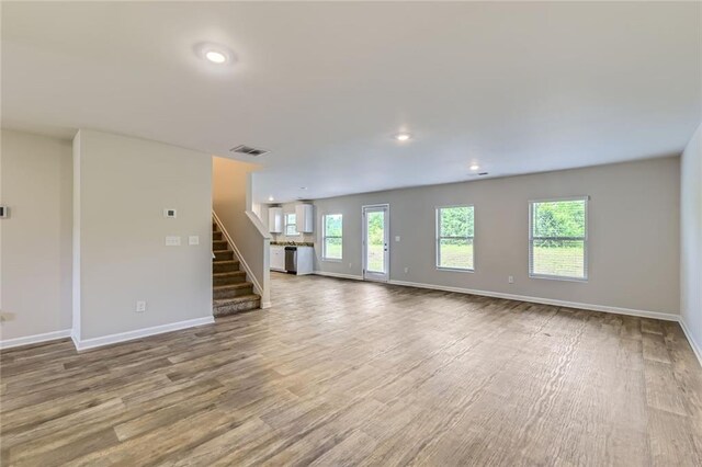 unfurnished living room with baseboards, visible vents, wood finished floors, and stairway