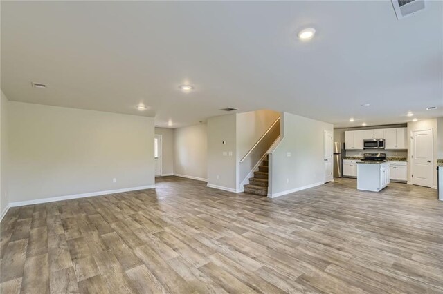 unfurnished living room featuring stairs, recessed lighting, baseboards, and light wood finished floors