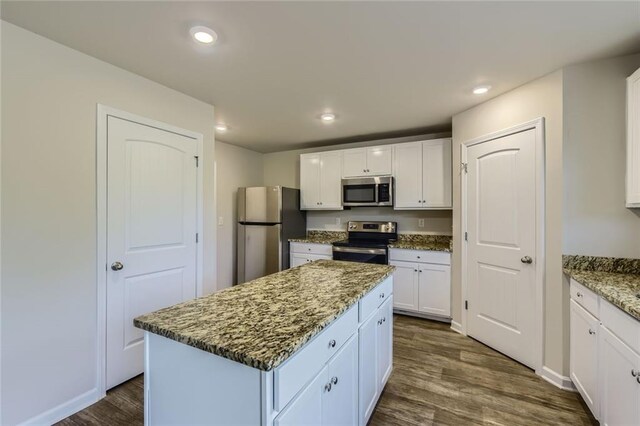 kitchen featuring dark wood-style flooring, a kitchen island, white cabinets, stone counters, and appliances with stainless steel finishes