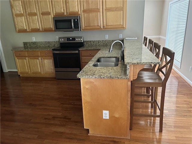 kitchen with a kitchen bar, kitchen peninsula, light stone counters, stainless steel appliances, and sink