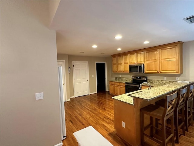 kitchen with light stone countertops, appliances with stainless steel finishes, kitchen peninsula, dark hardwood / wood-style floors, and a breakfast bar area