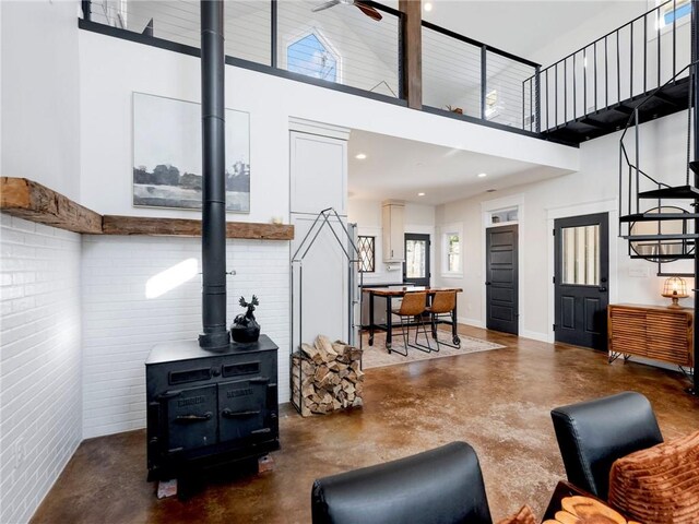 living room with finished concrete flooring, recessed lighting, a high ceiling, a wood stove, and baseboards