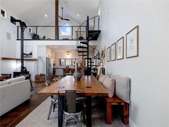 dining space featuring ceiling fan, high vaulted ceiling, visible vents, baseboards, and stairs